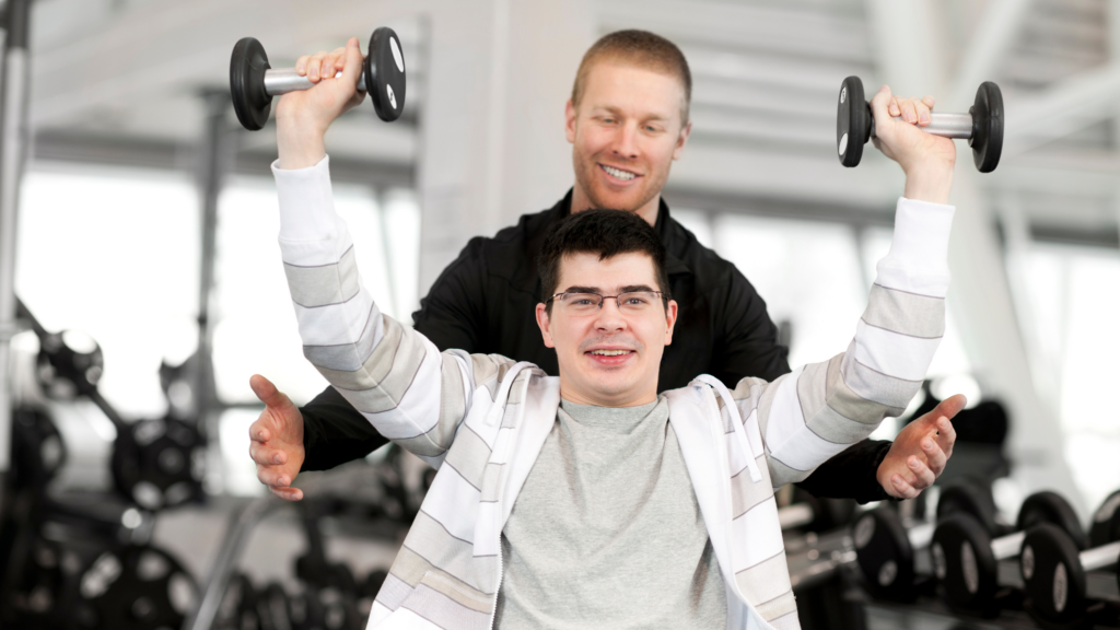Young man with disability lifting weights with personal trainer in gym